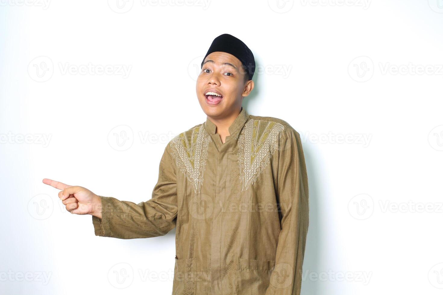 surprised asian muslim man wearing islamic clothes pointing to copy space isolated in white background photo