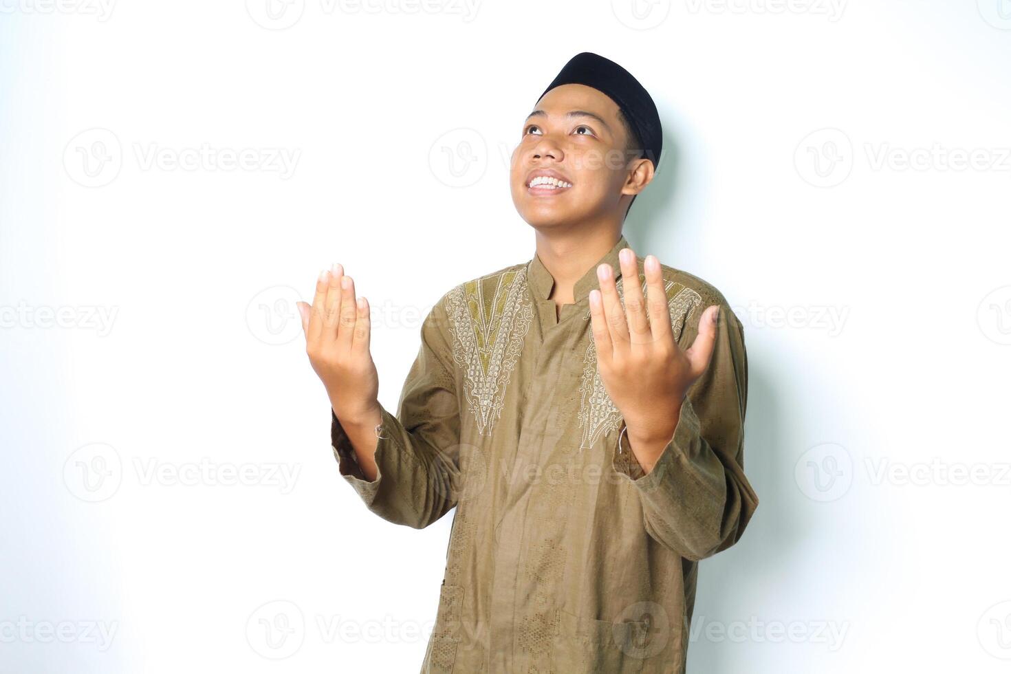 smiling asian muslim man wearing islamic clothes praying in ramadhan isolated on white background photo