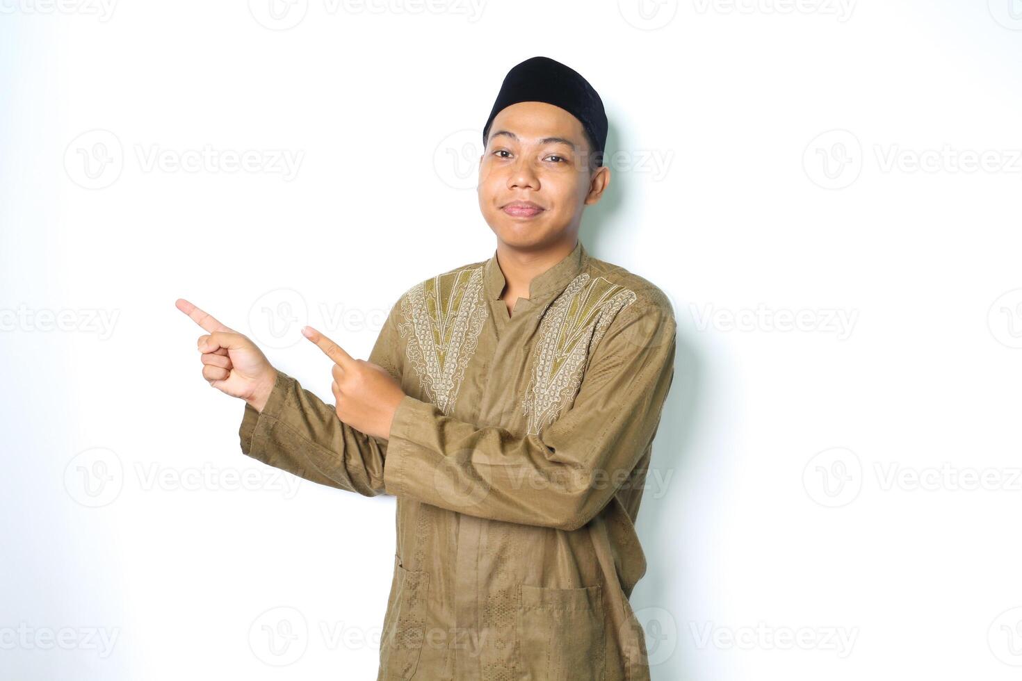 calma asiático musulmán hombre sonriente a cámara vistiendo koko ropa señalando a junto a aislado en blanco antecedentes foto