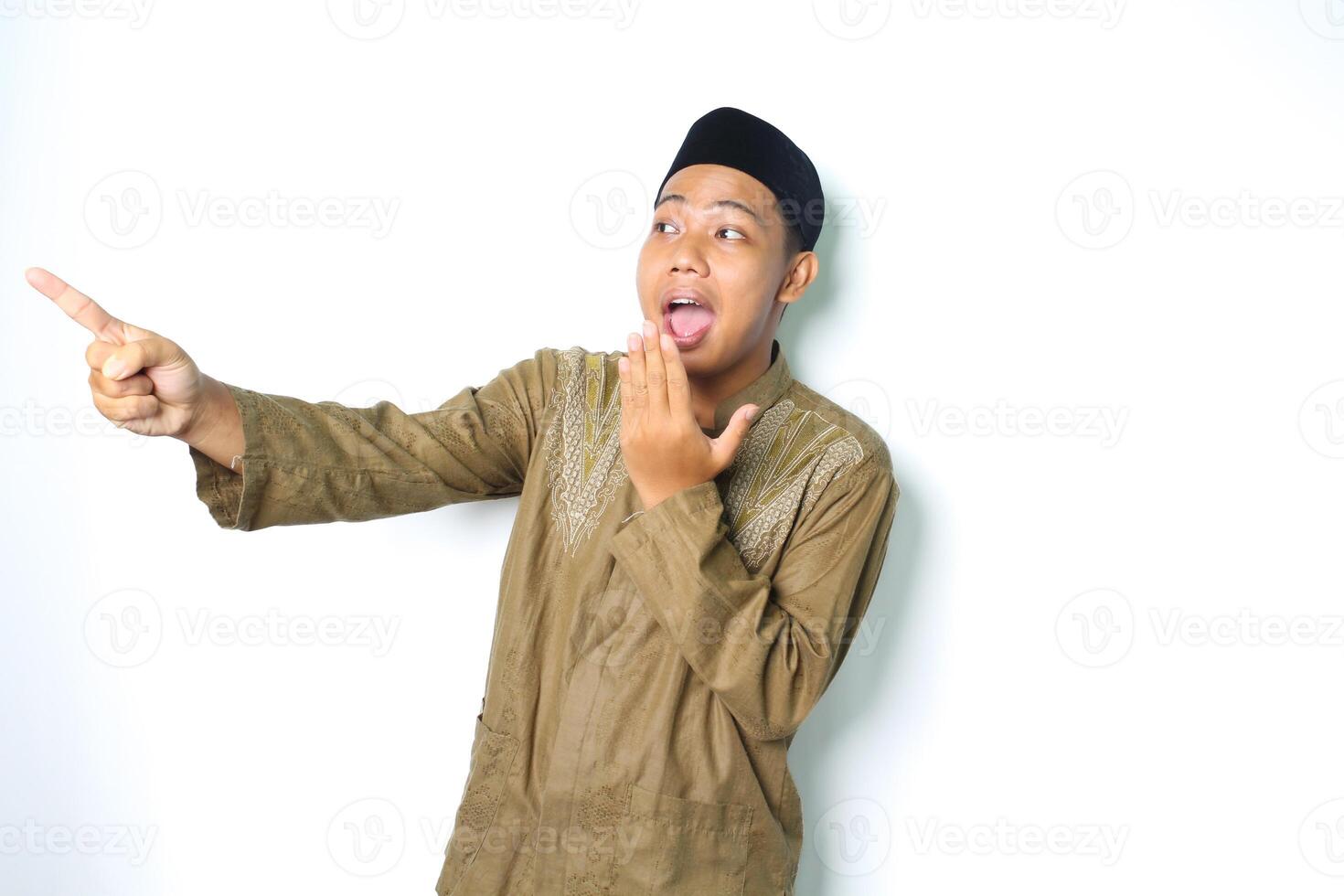 shocked asian muslim man pointing to beside with covering open mouth isolated on white background photo