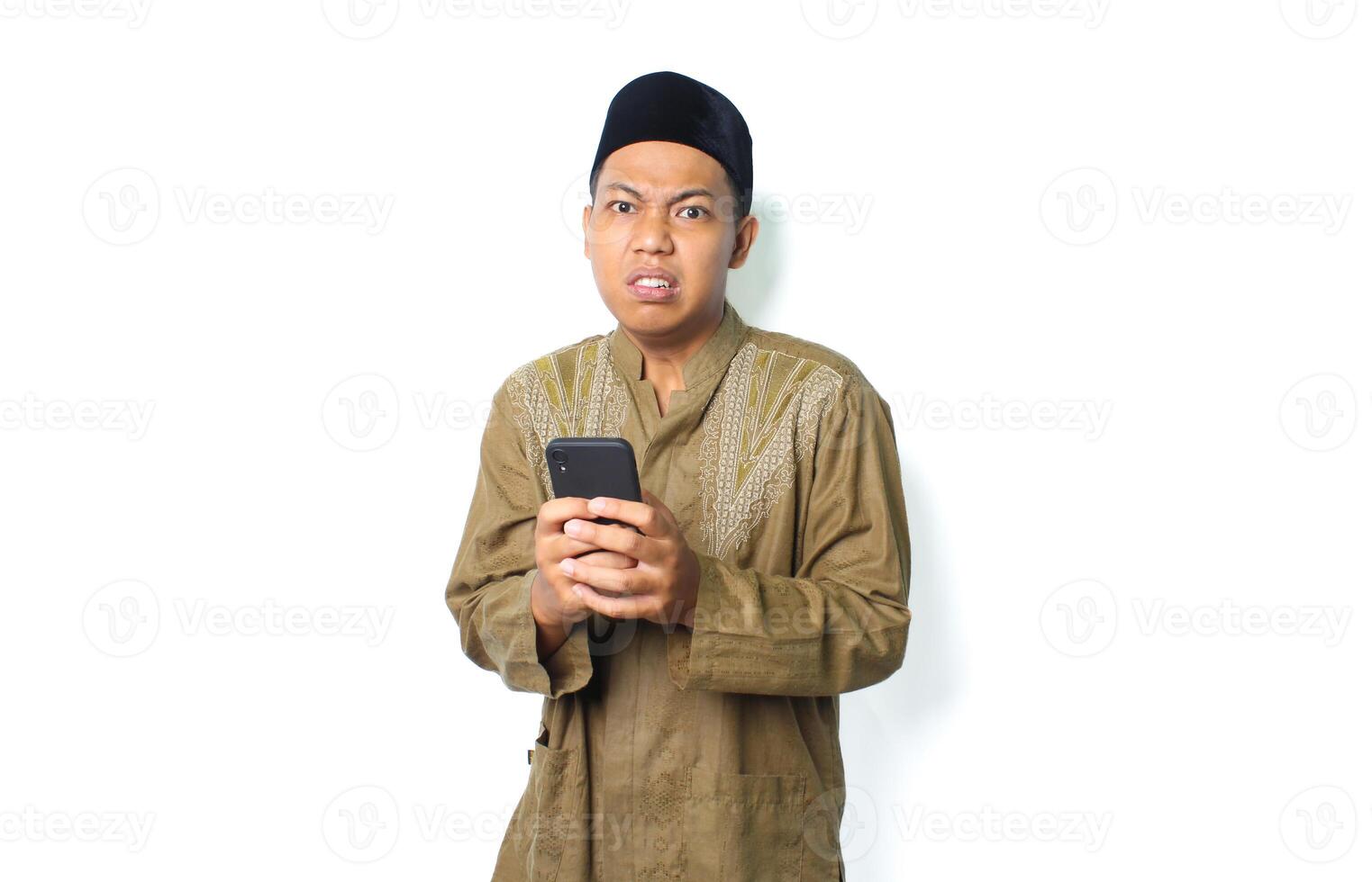 angry asian muslim man wearing islamic dress holding mobile phone isolated on white background photo
