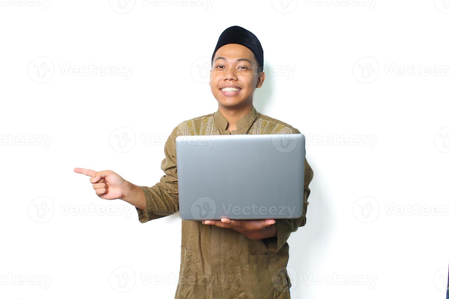 sonriente asiático musulmán hombre participación ordenador portátil señalando a junto a aislado en blanco antecedentes foto