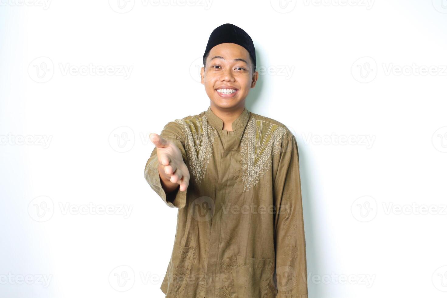 friendly smiling asian muslim man stretching hand at camera to offer handshake for forgiveness in eid mubarak celebration isolated on white background photo