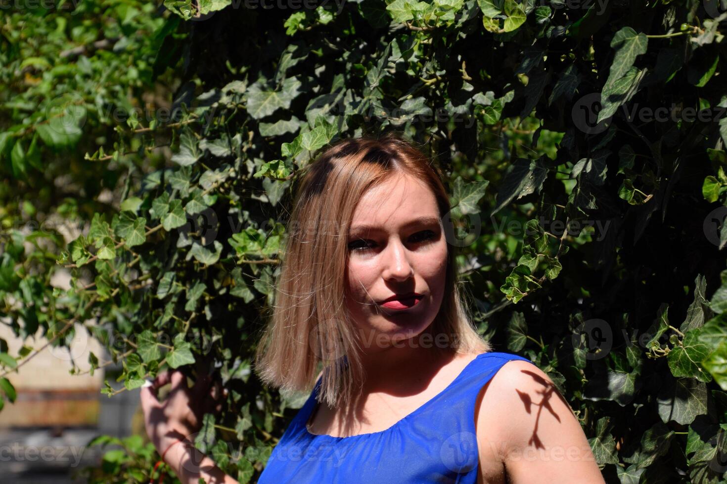 Portrait of a girl in a blue dress on background of green arbor of ivy. photo