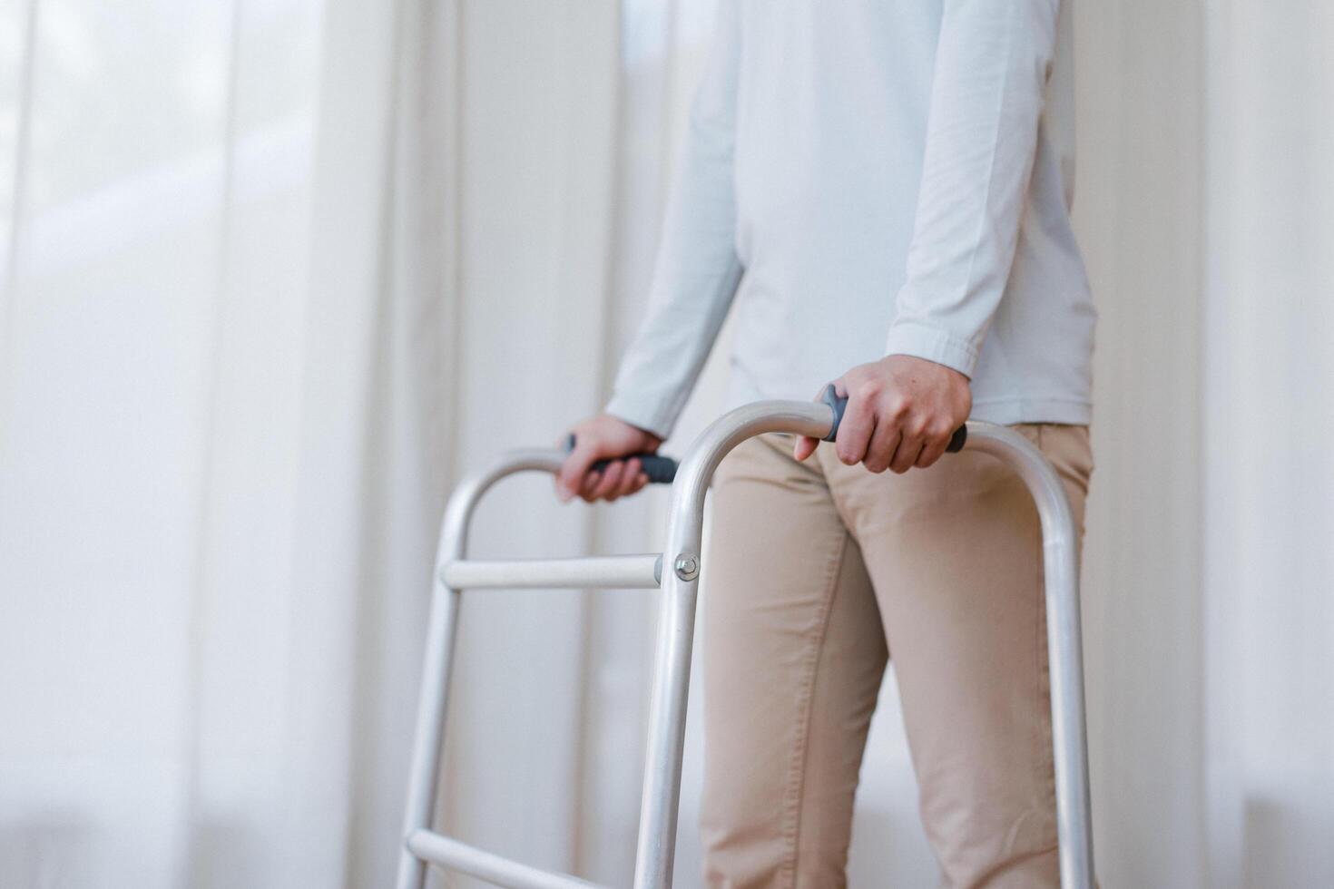 recortado ver de mayor hombre caminando con marco a hogar, de cerca. joven masculino asiático utilizando médico equipo a moverse alrededor su casa. discapacitado más viejo persona en necesitar de profesional ayuda foto