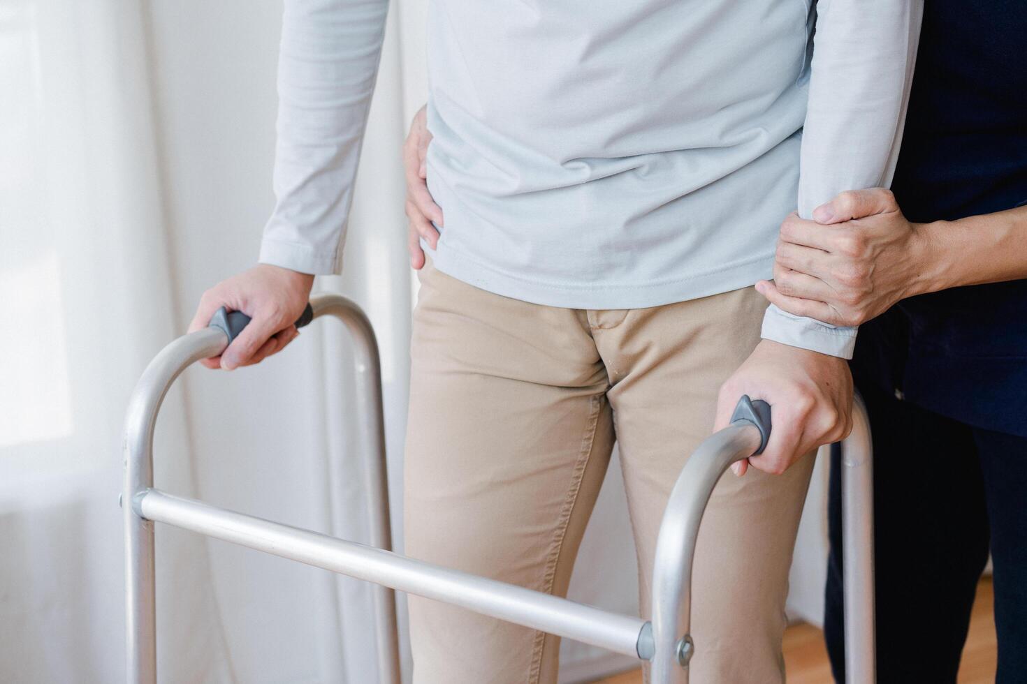 Cropped view of elderly man walking with frame at home, closeup. young male asian using medical equipment to move around his house. Disabled older person in need of professional help photo