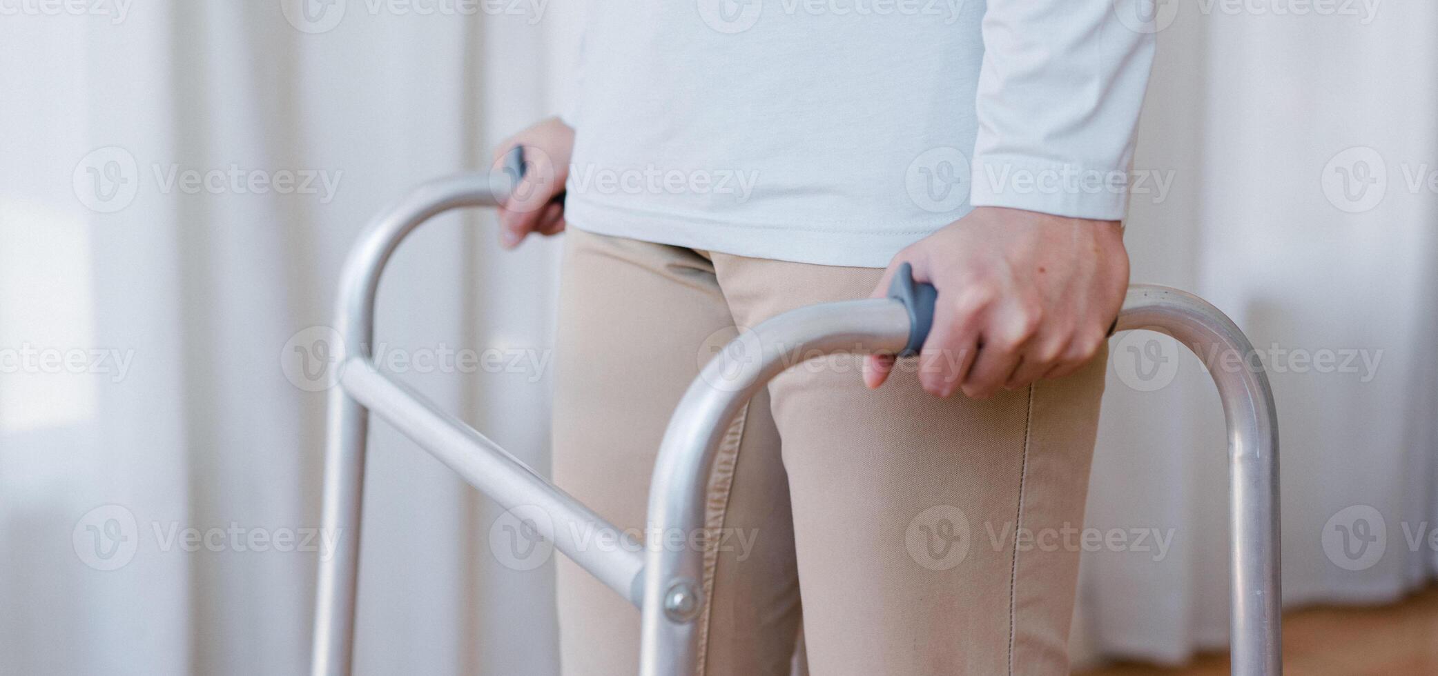 Cropped view of elderly man walking with frame at home, closeup. young male asian using medical equipment to move around his house. Disabled older person in need of professional help photo