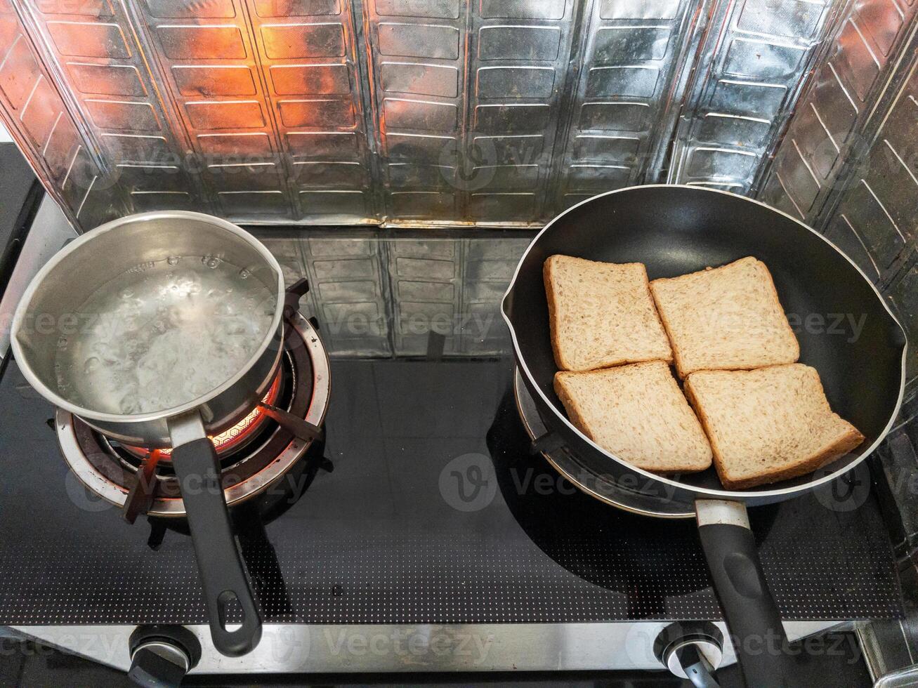 A pot of boiling water and bread toast on a Teflon pan. photo