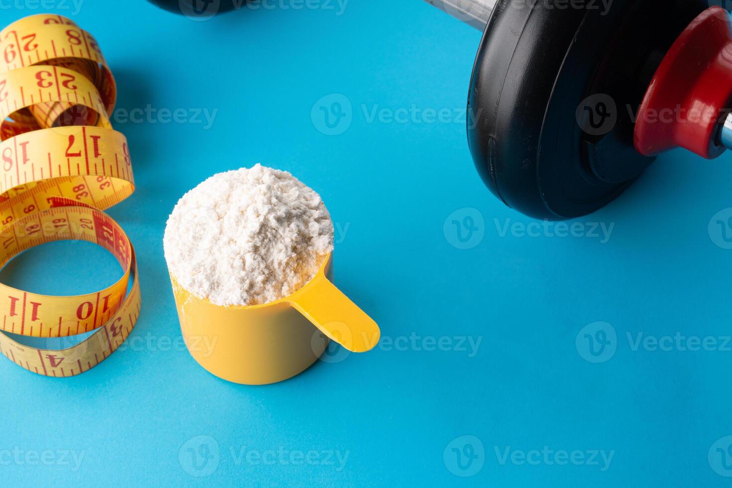 A scoop of creatine next to a dumbbell and a tape measure on a blue background. photo