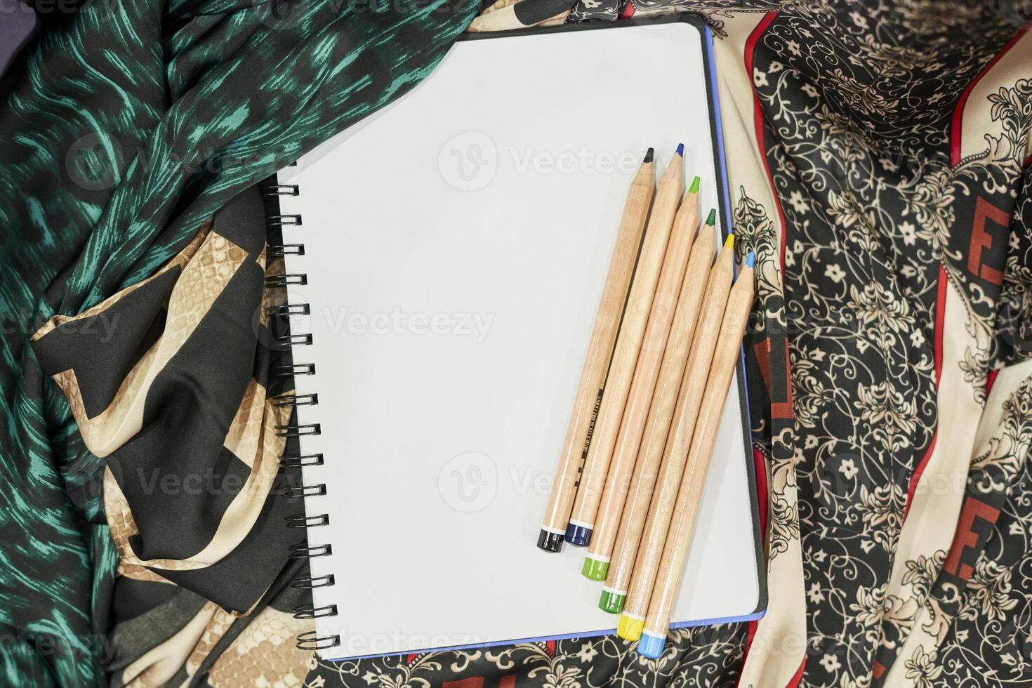 a notebook, pencils and a scarf on a table photo