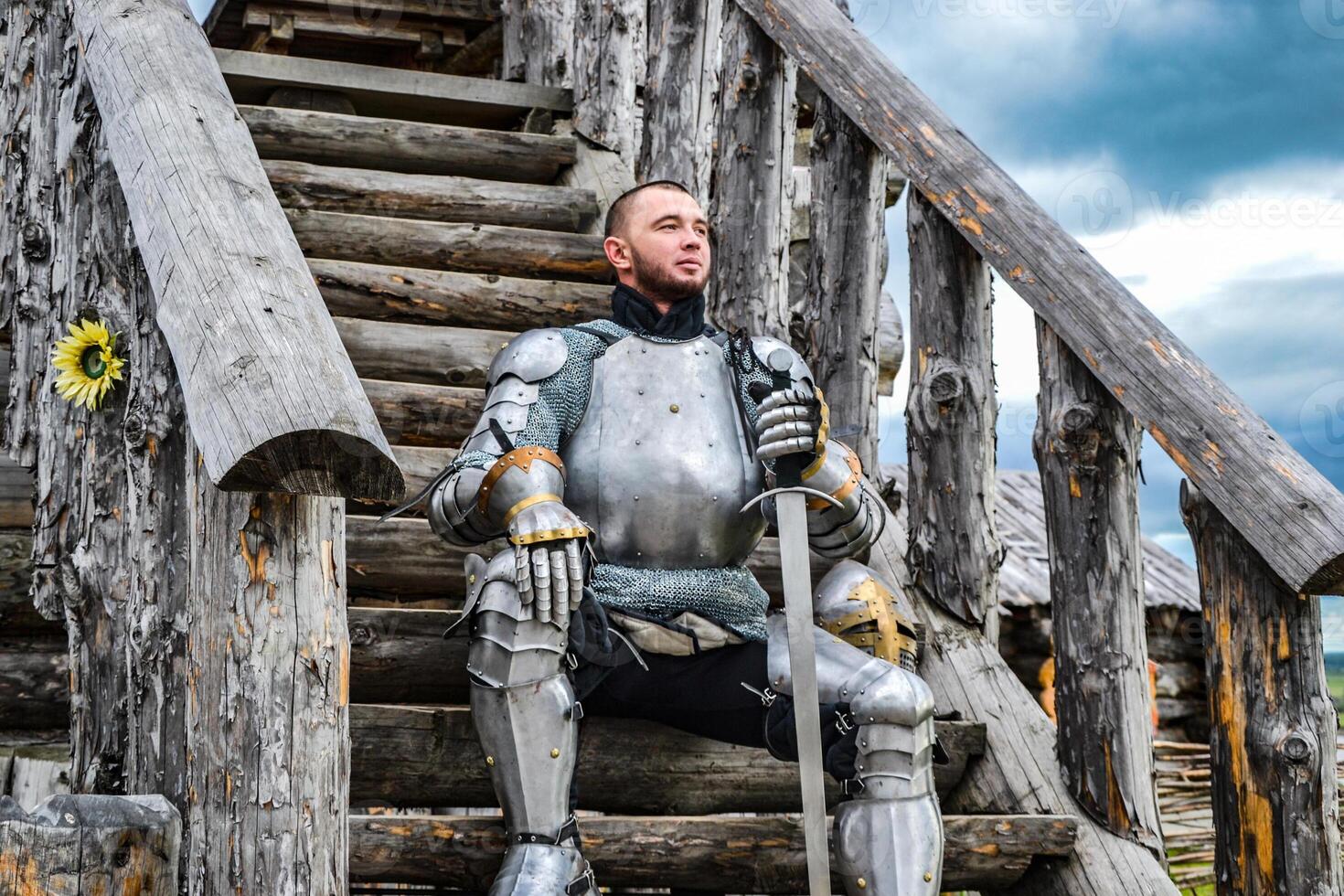 Knight in the armor on the wooden steps. Knightly armor and weapon photo