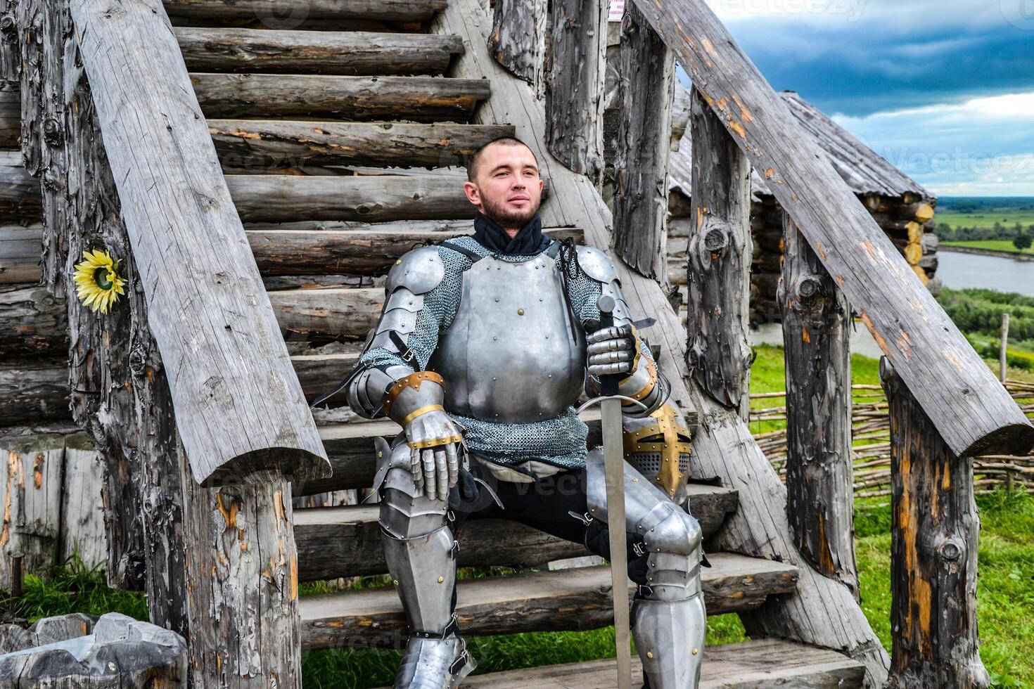 Knight in the armor on the wooden steps. Knightly armor and weapon photo