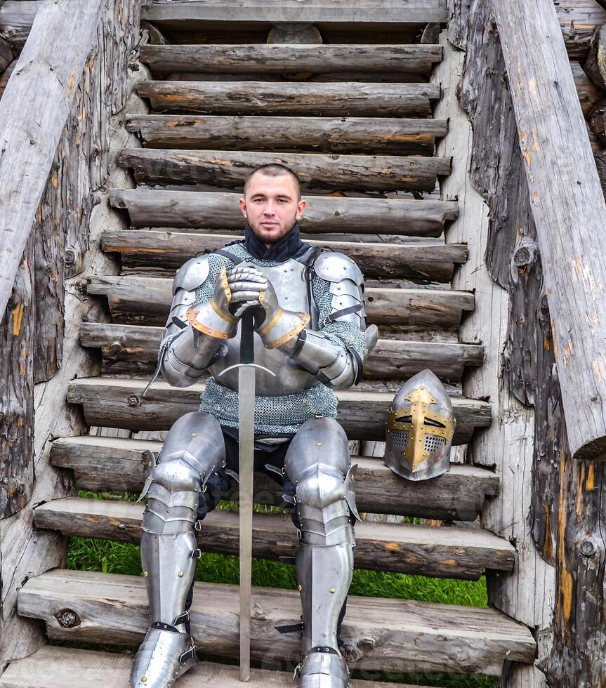 Knight in the armor on the wooden steps. Knightly armor and weapon photo