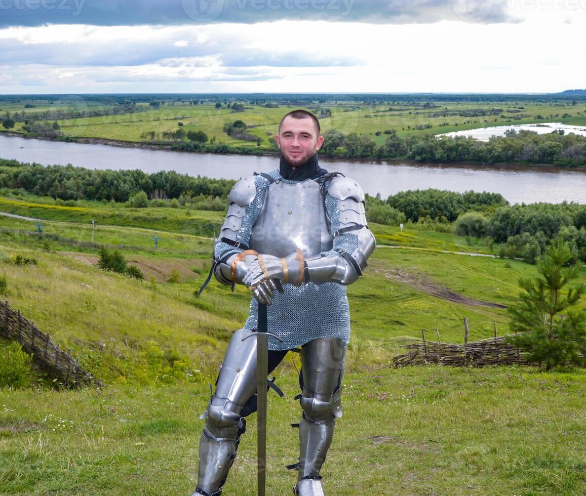 knight in armor stands against the background of native open spaces, forests and a river. Knightly armor and weapon photo