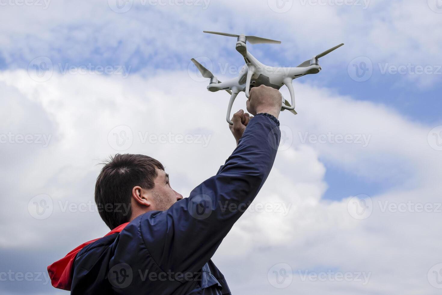 A man with a quadrocopter in his arms raised to the sky. A white photo
