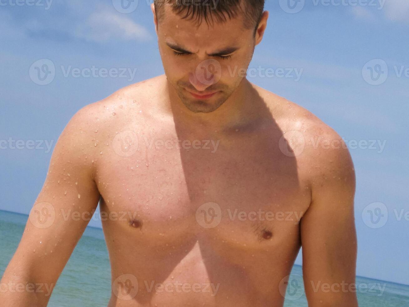 Male torso. A muscular young man stands on the beach. photo