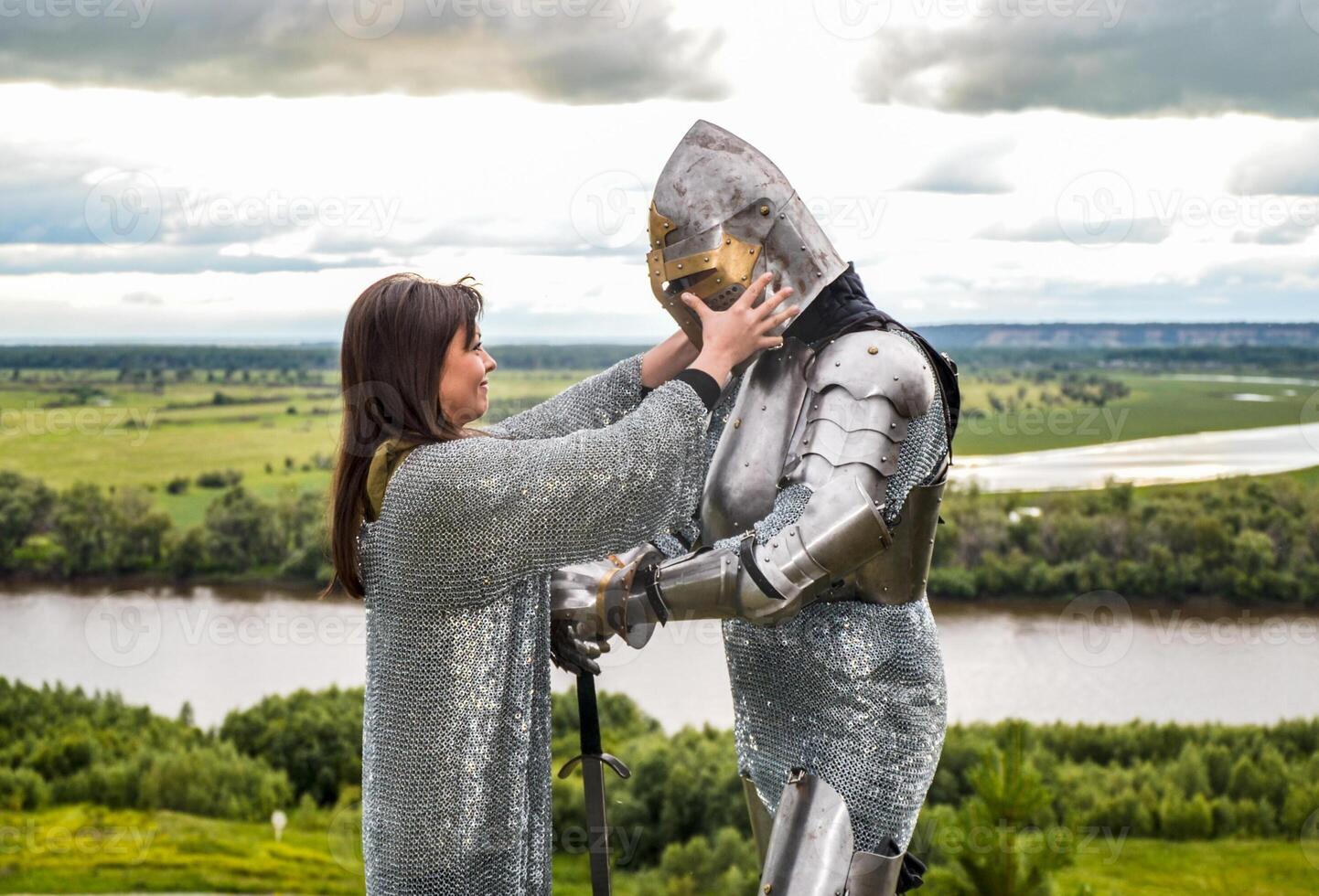 The lady puts on her knight a helmet. Knightly armor and weapon photo