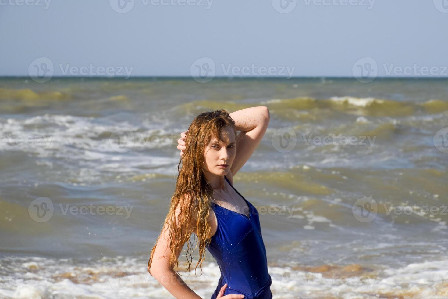 A blonde girl in a blue bathing suit on the beach. Beach holidays. photo