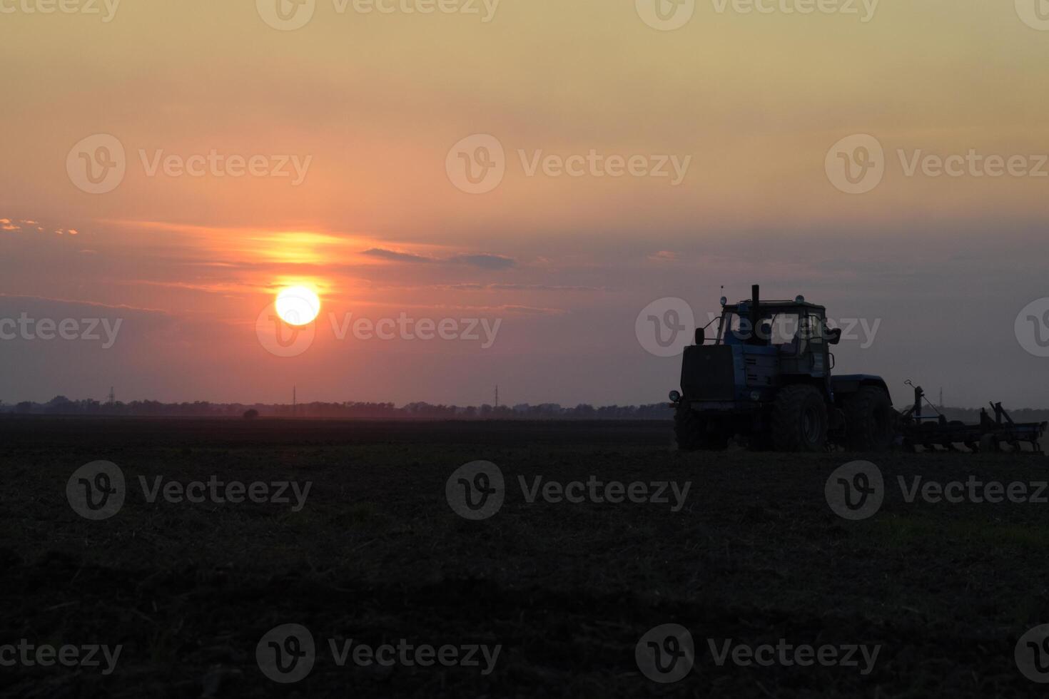 Tractor plowing plow the field on a background sunset. tractor silhouette on sunset background photo
