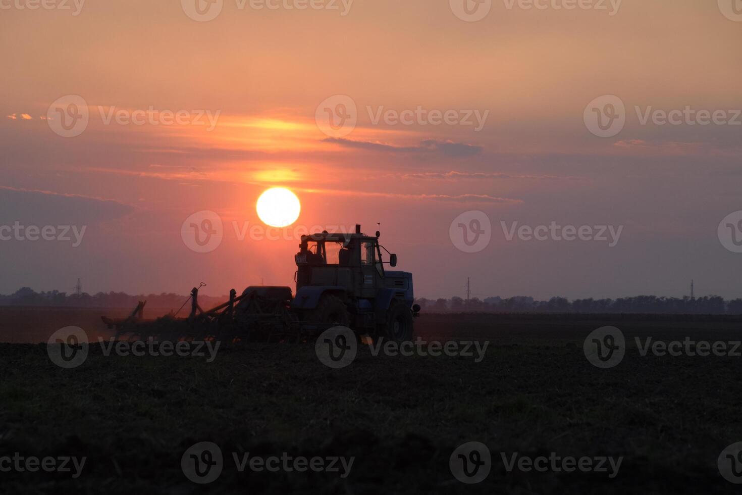 Tractor plowing plow the field on a background sunset. tractor silhouette on sunset background photo