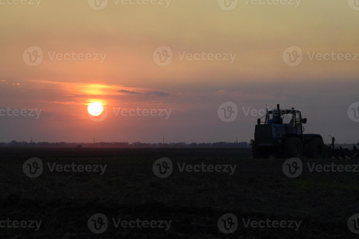 Tractor plowing plow the field on a background sunset. tractor silhouette on sunset background photo