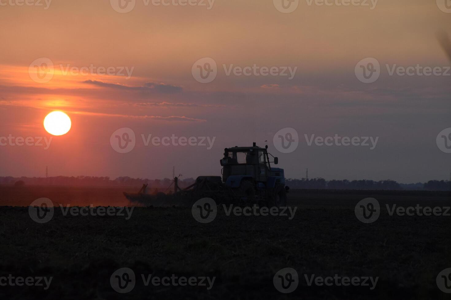 Tractor plowing plow the field on a background sunset. tractor silhouette on sunset background photo