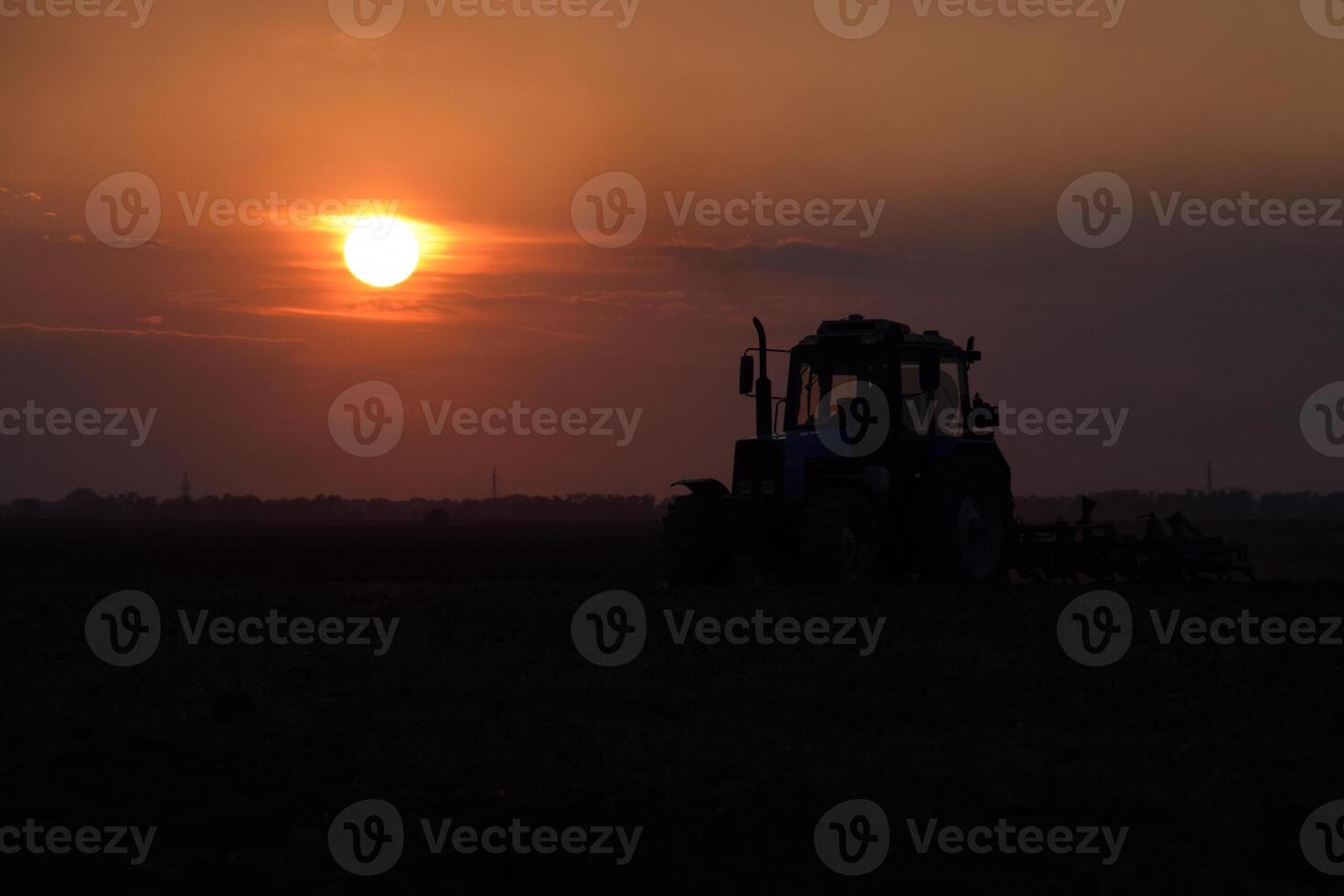Tractor plowing plow the field on a background sunset. tractor silhouette on sunset background photo