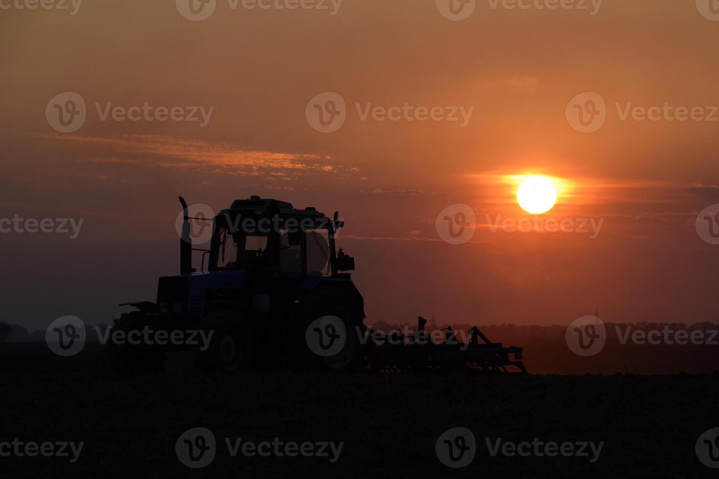 Tractor plowing plow the field on a background sunset. tractor silhouette on sunset background photo