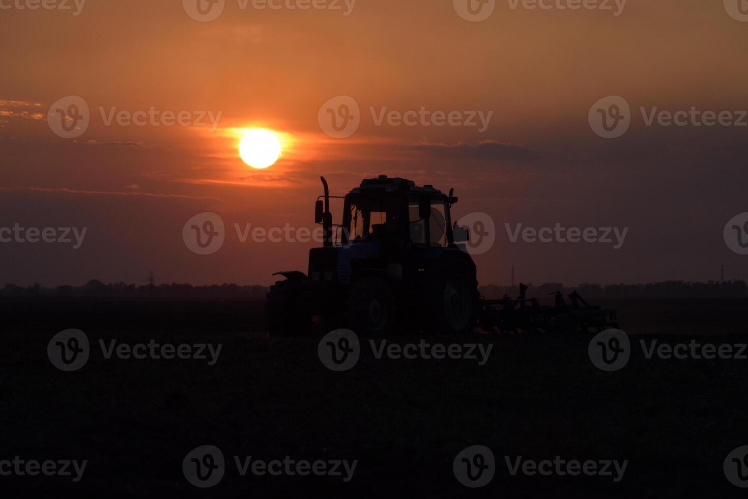 Tractor plowing plow the field on a background sunset. tractor silhouette on sunset background photo