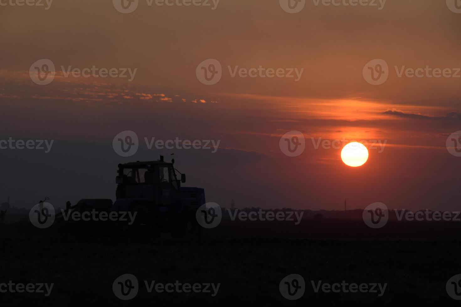 Tractor plowing plow the field on a background sunset. tractor silhouette on sunset background photo