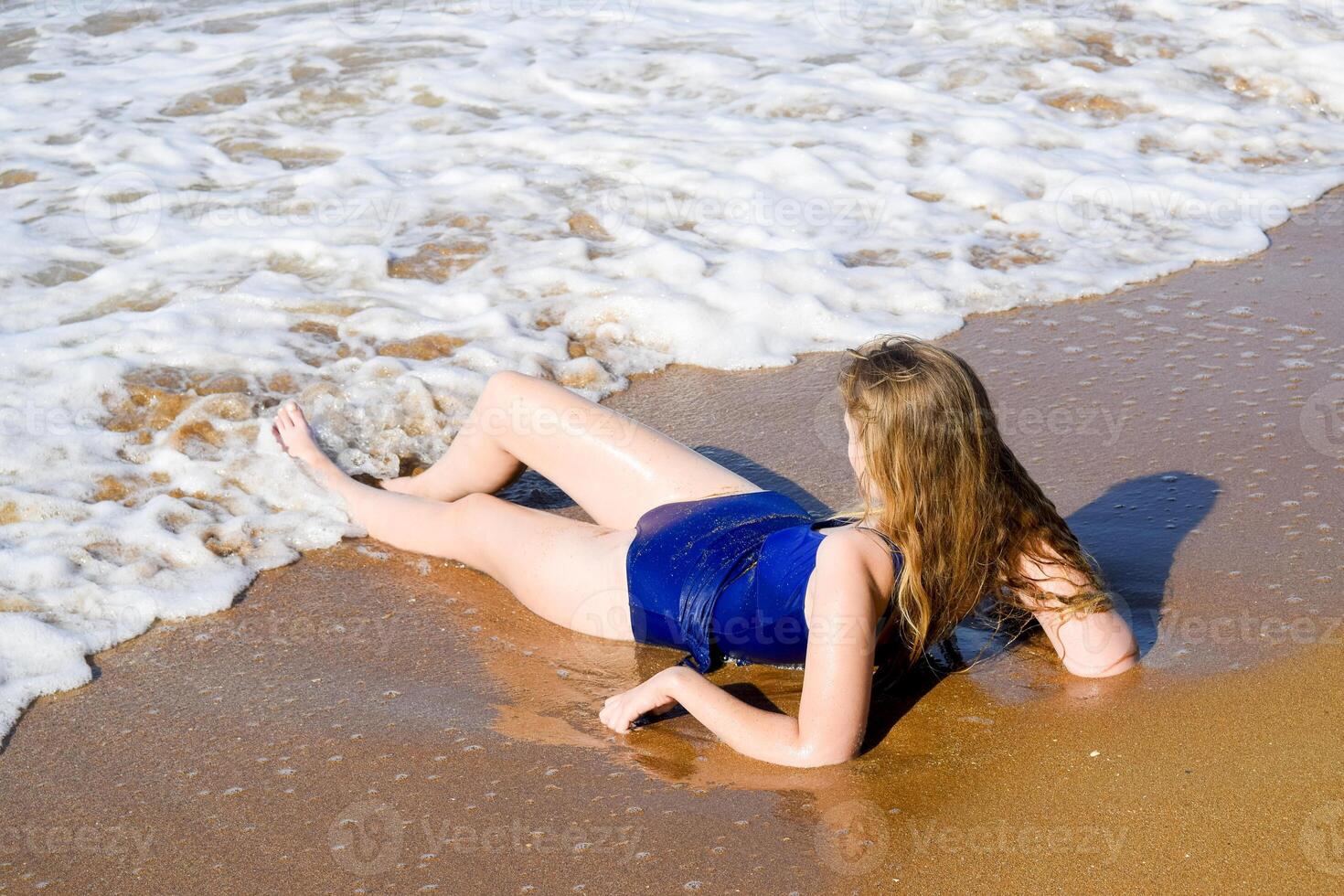 Girl in a blue bathing suit lies on the seashore and relaxes. Waves caress the girl's body photo
