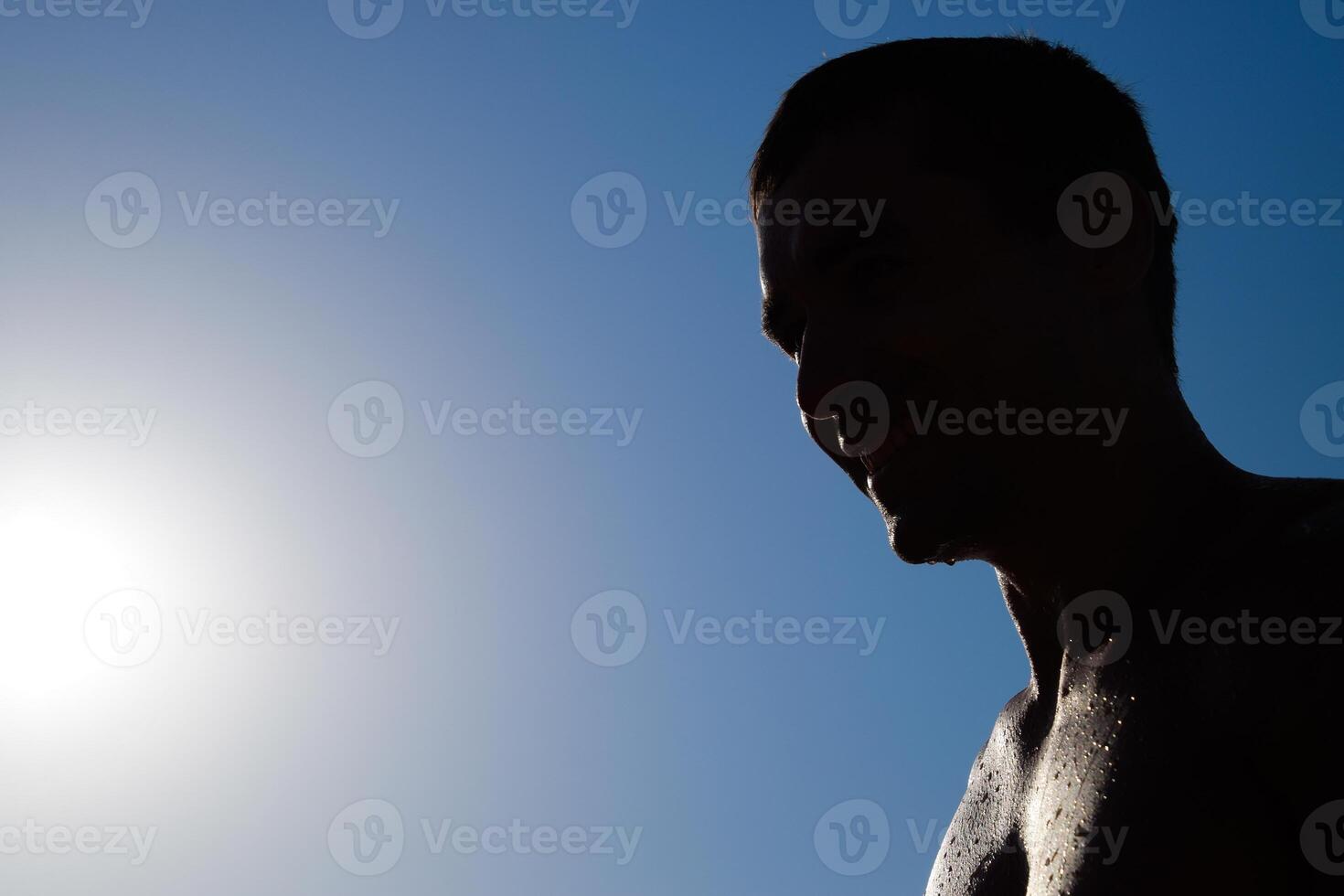 Silhouette of a man against a blue sky and sun. A man in drops of sea water photo