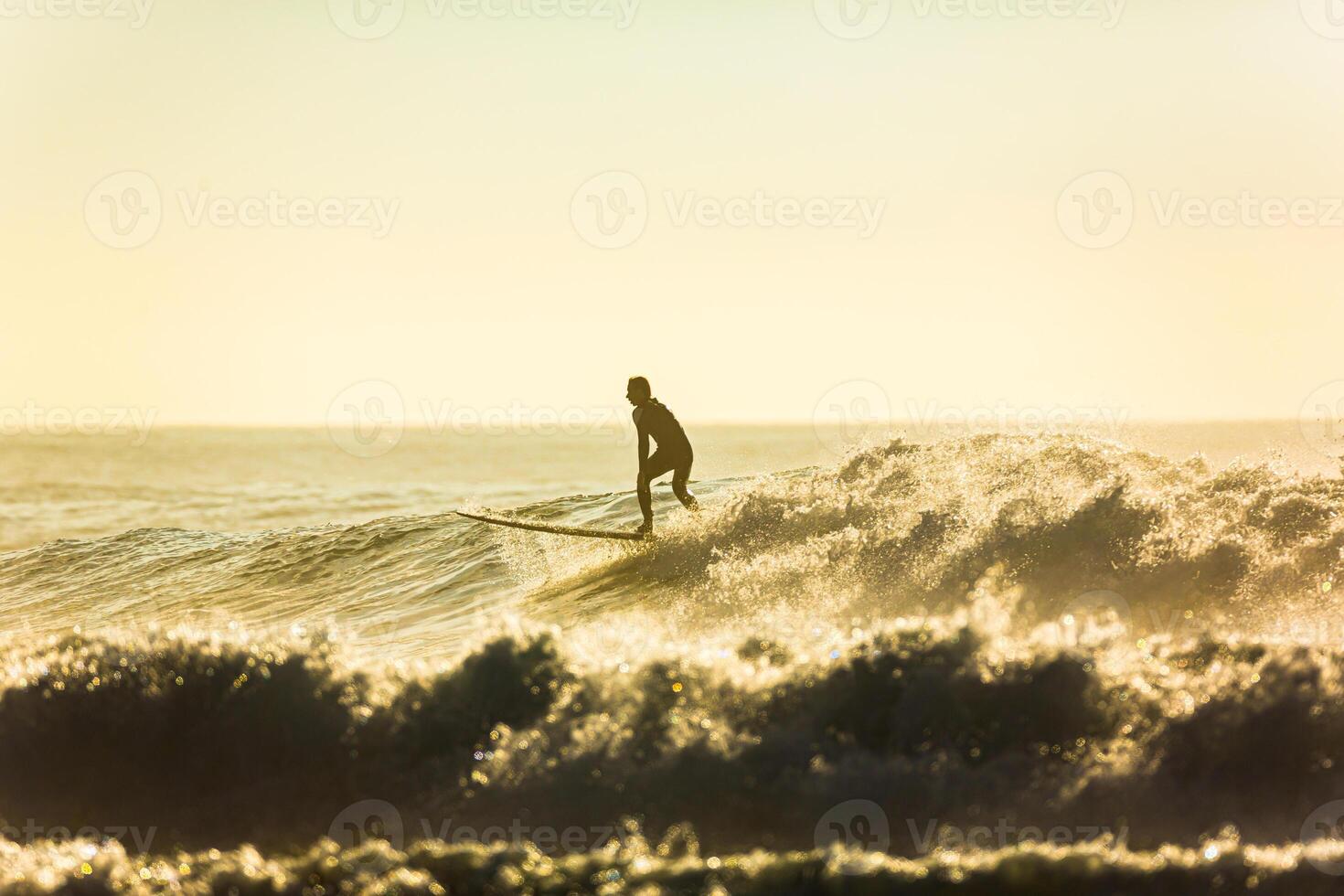 An unidentified surfer rides a big wave with foam at sunset photo