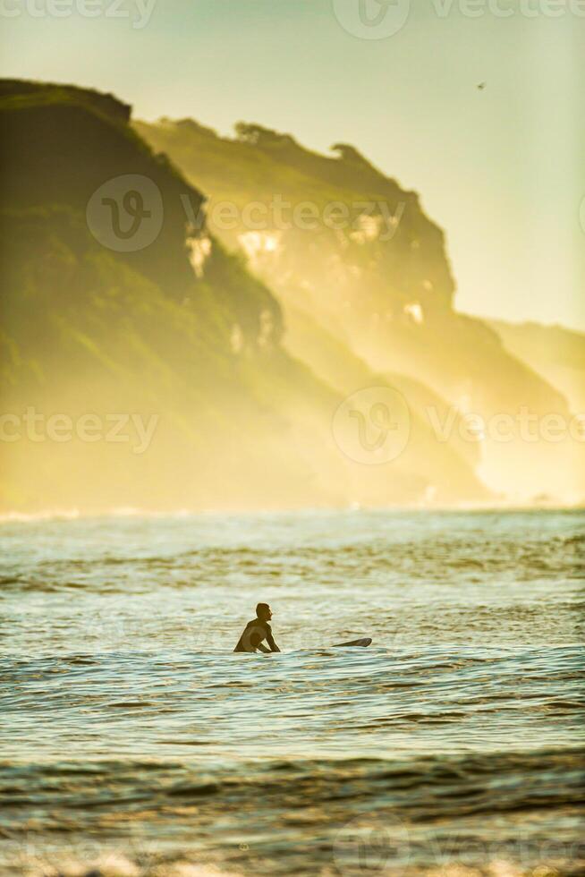 Silhouette of a surfer waiting for a big wave sitting on the board at dawn photo