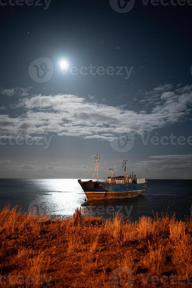 abandoned ship under a full moon sky, long exposure at night photo