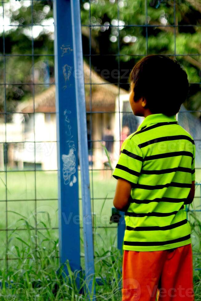 pequeño niño en el banquillo visto desde detrás mirando dentro el fútbol americano campo foto