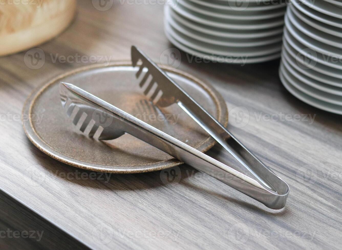 Image subject of stainless steel kitchen tongs on a plate. photo