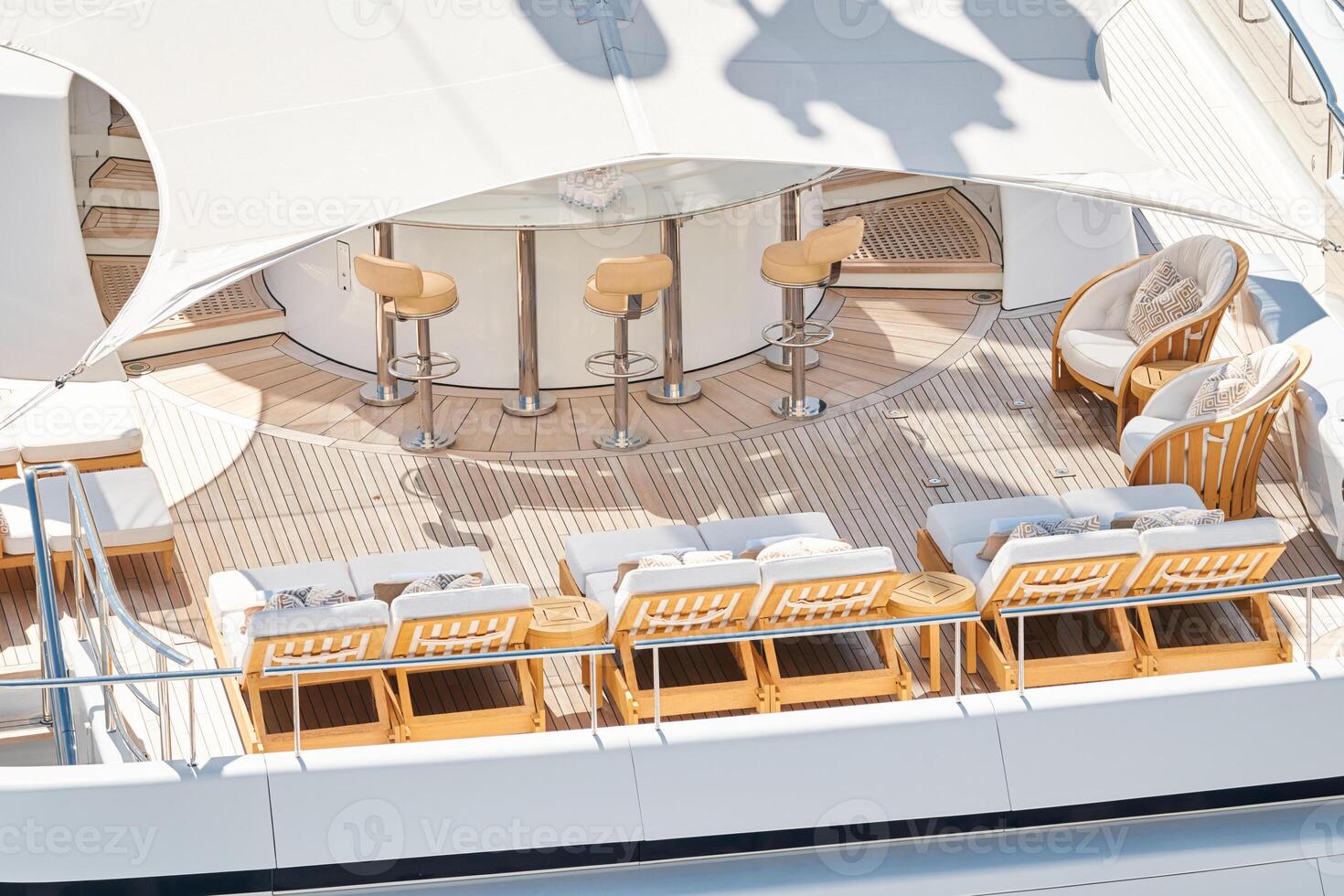 Close up footage of a relaxation area on the open teak deck of an expensive megayacht at sunny day, with awnings stretched over the deck to protect from the sun, wealth life, table and chairs photo