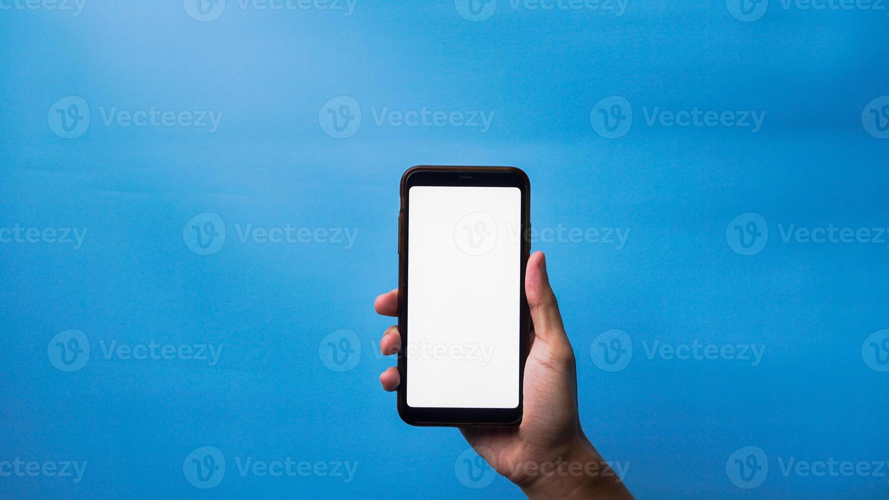 Hand of man holding mobile smartphone and showing blank phone screen on blue background photo