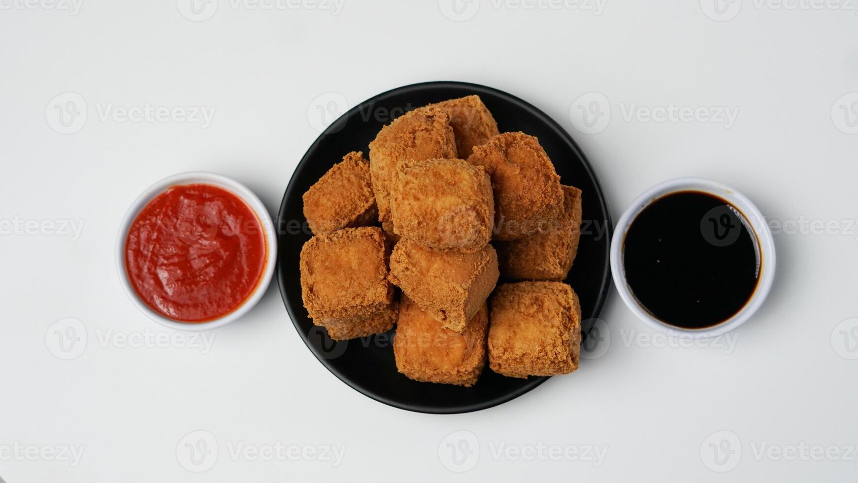 Fried tofu on a black plate with chili sauce and sweet soy sauce on a white background photo