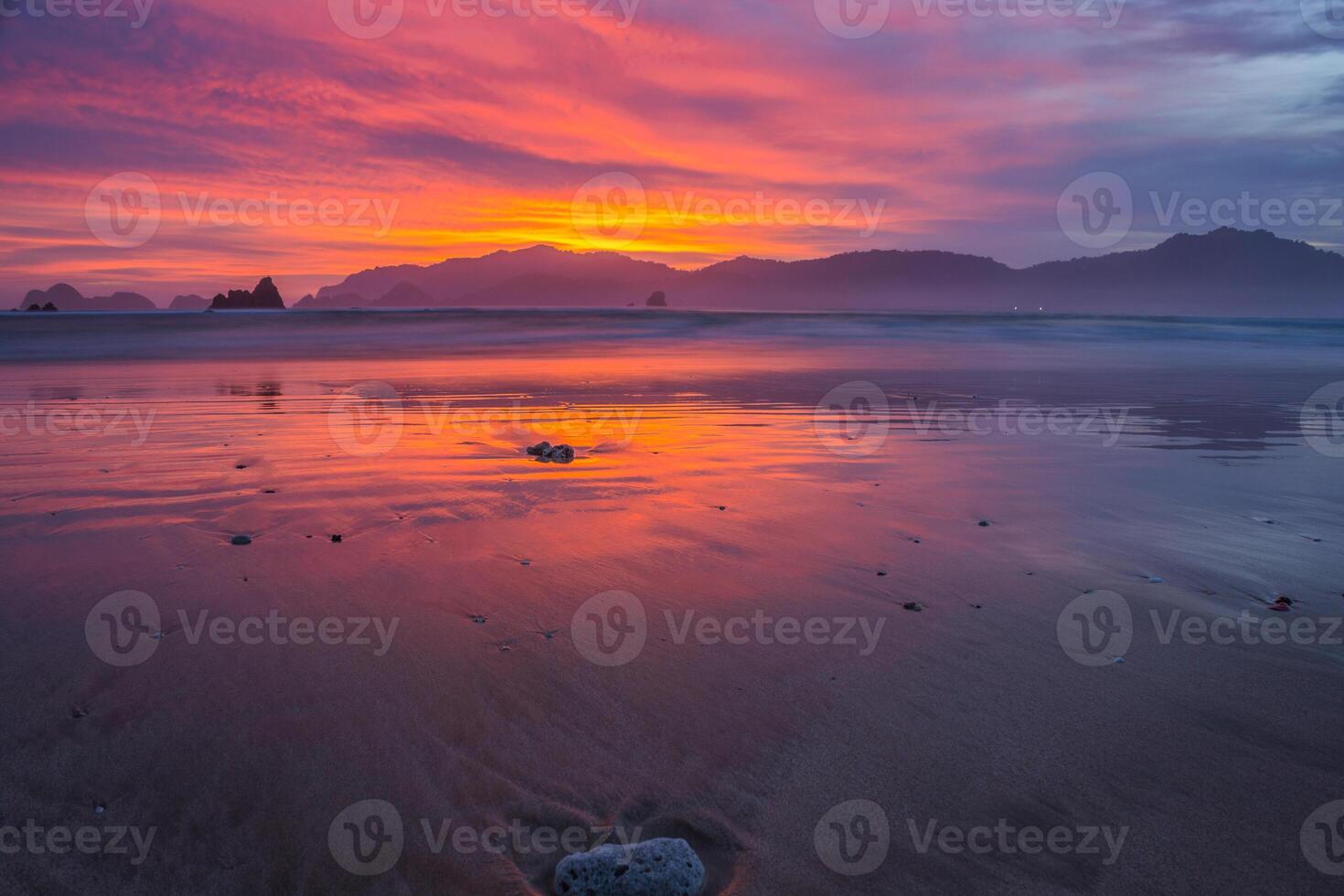 Sunset on the beach with red-orange sky reflected on wet sands. Scenic view of sunset in Banyuwangi, Indonesia photo