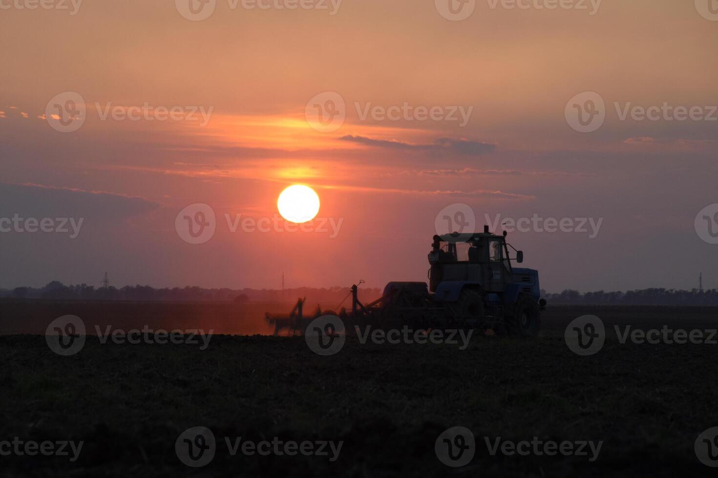 Tractor plowing plow the field on a background sunset. tractor silhouette on sunset background photo
