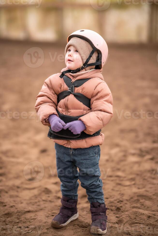 Portrait of little girl in protective jacket and helmet before riding lesson. High quality photo