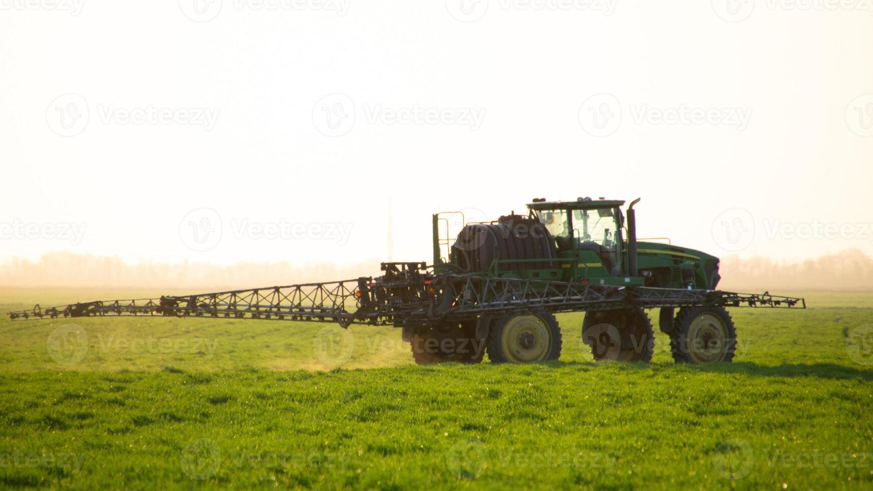 Tractor on the sunset background. Tractor with high wheels is making fertilizer on young wheat. photo