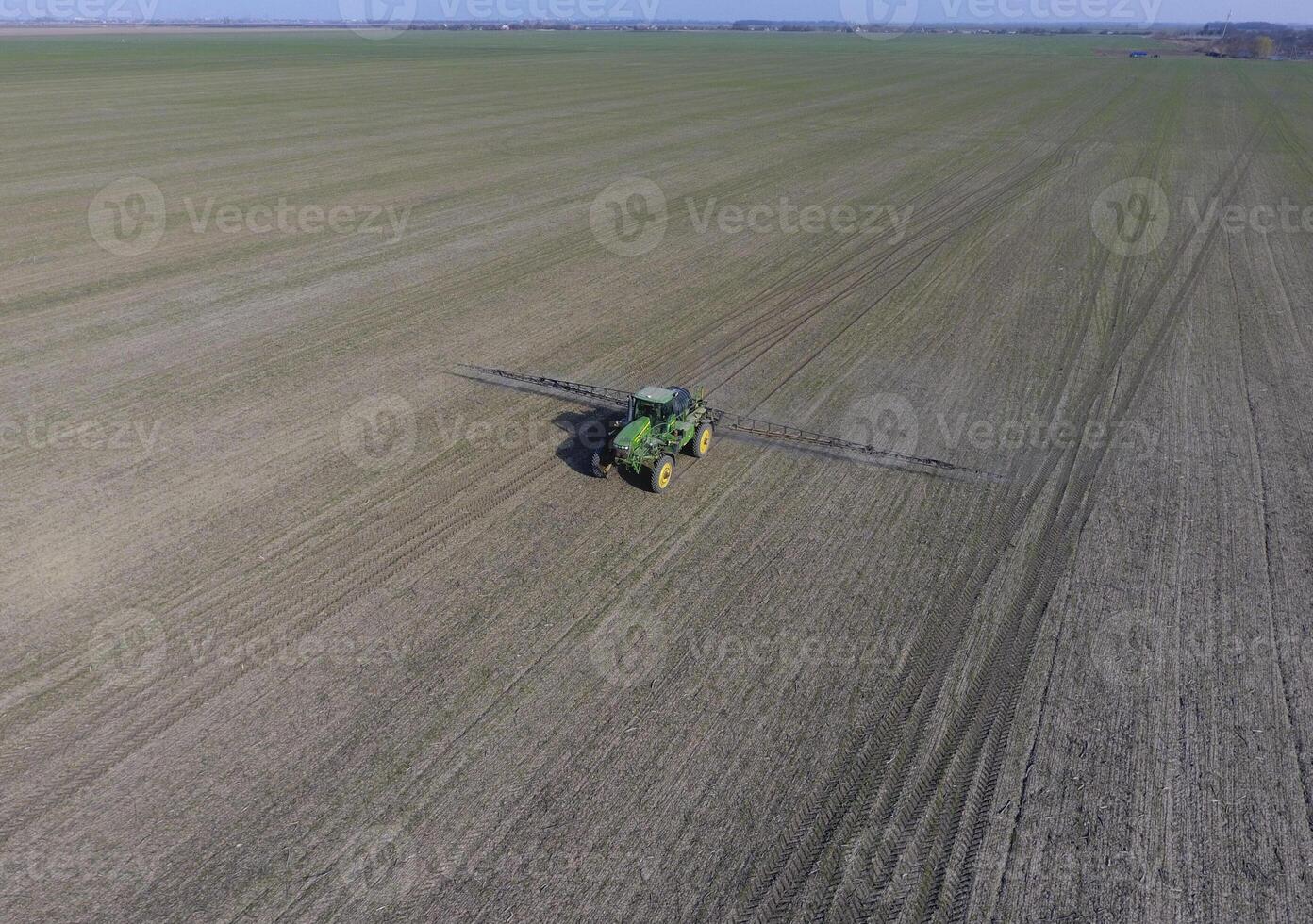 Tractor with hinged system of spraying pesticides. Fertilizing with a tractor, in the form of an aerosol, on the field of winter wheat. photo