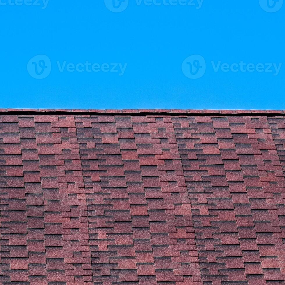 Roof from multi-colored bituminous shingles. Patterned bitumen shingles. Bituminous burgundy roof. photo