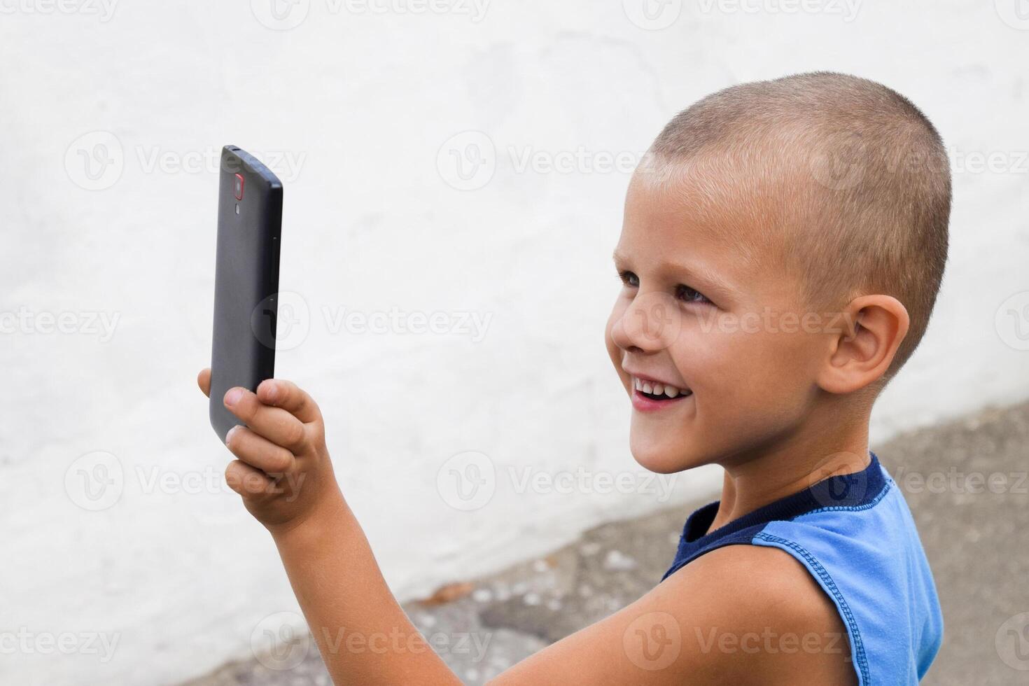 niño con un teléfono inteligente un pequeño chico dispara vídeo en un teléfono inteligente foto