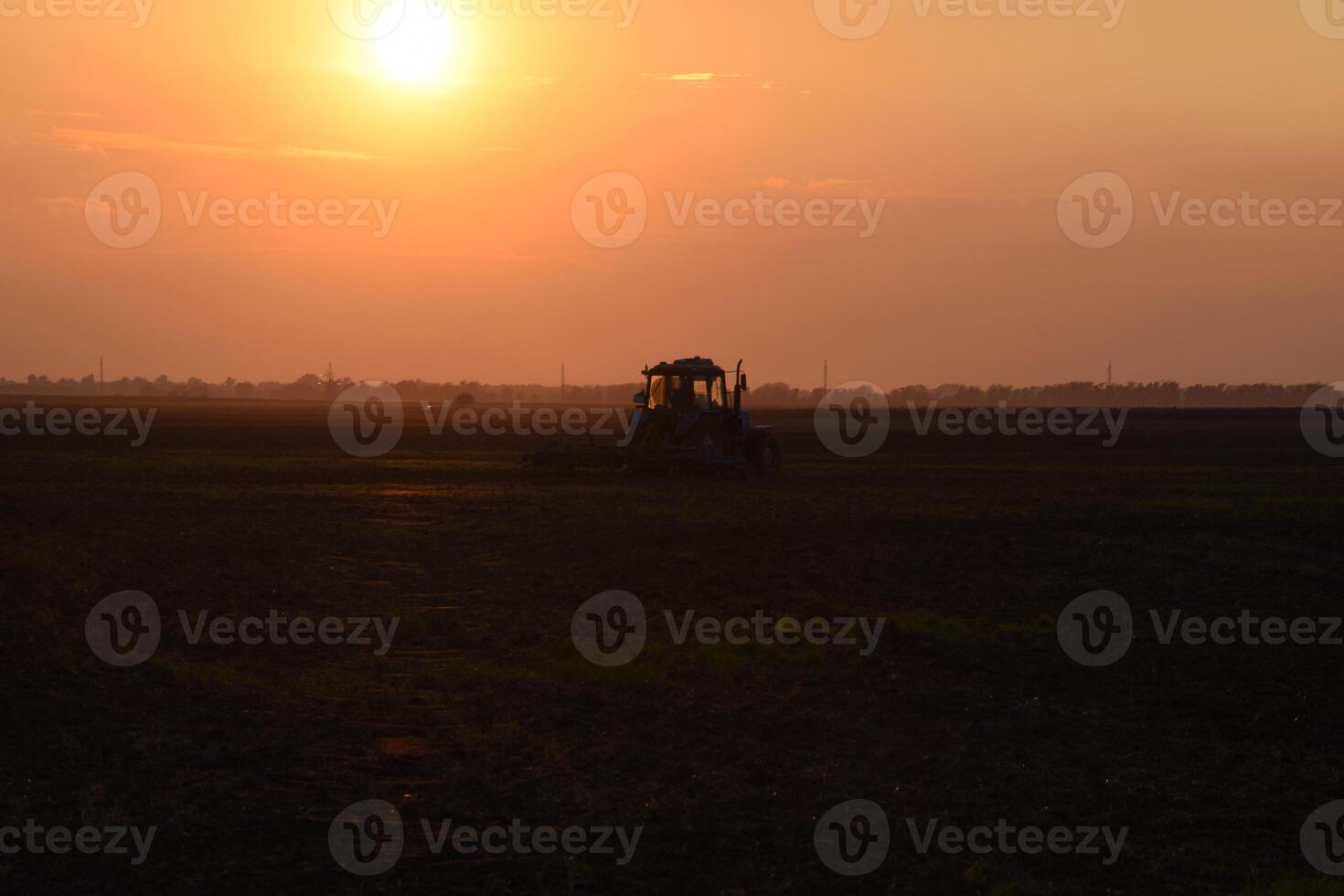 Tractor plowing plow the field on a background sunset. tractor silhouette on sunset background photo