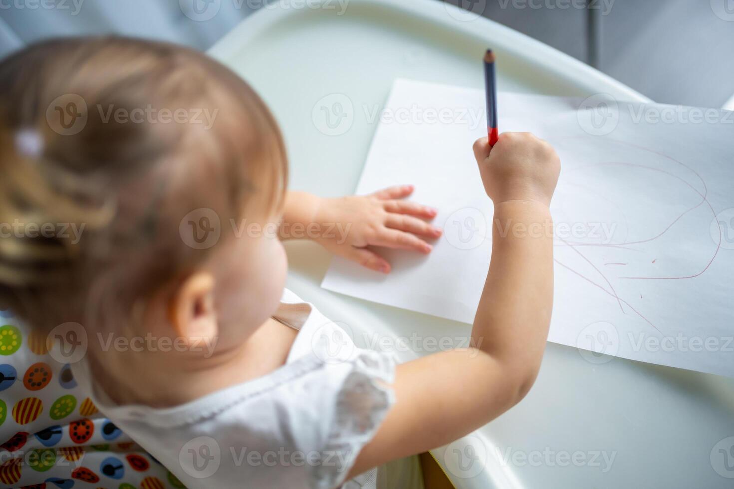 Cute little girl painting with red pencil at home. Creative games for kids. Stay at home entertainment photo