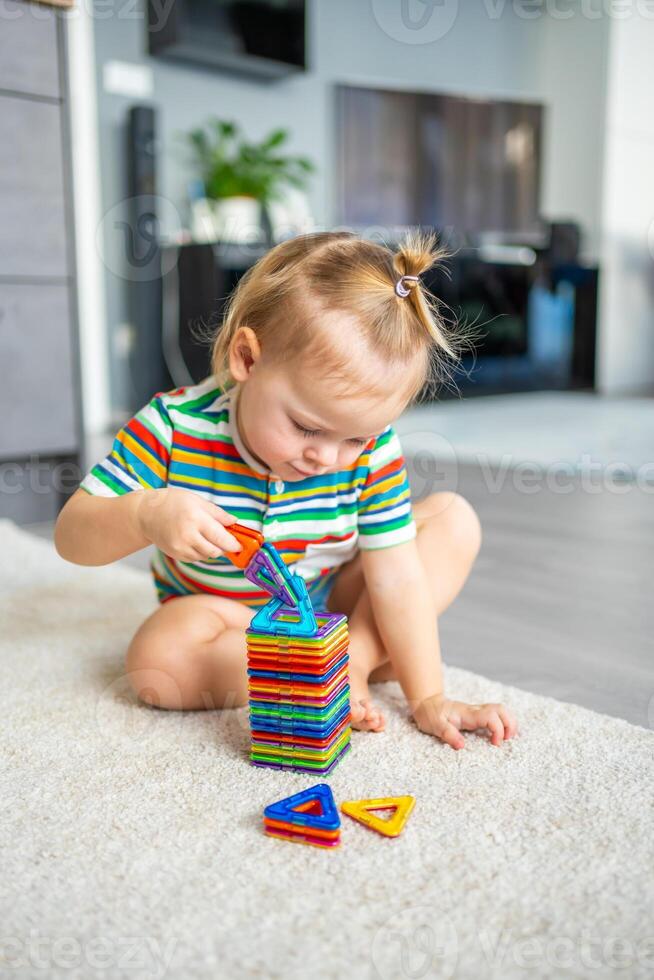 pequeño niña jugando vistoso imán el plastico bloques equipo a hogar. el niño jugando educativo juegos. temprano infancia desarrollo. foto